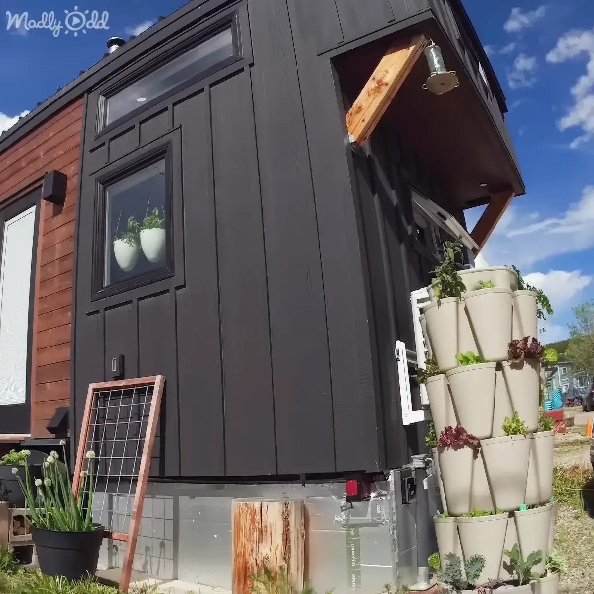 A modern tiny house with dark gray siding, a solar panel, and a vertical garden of white pots stacked on the side.