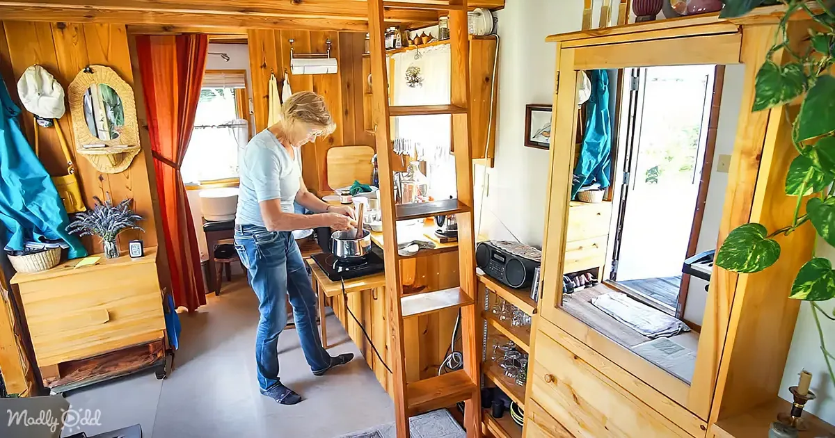 A woman cooks in a cozy, wooden cabin kitchen with shelves, plants, and a window.