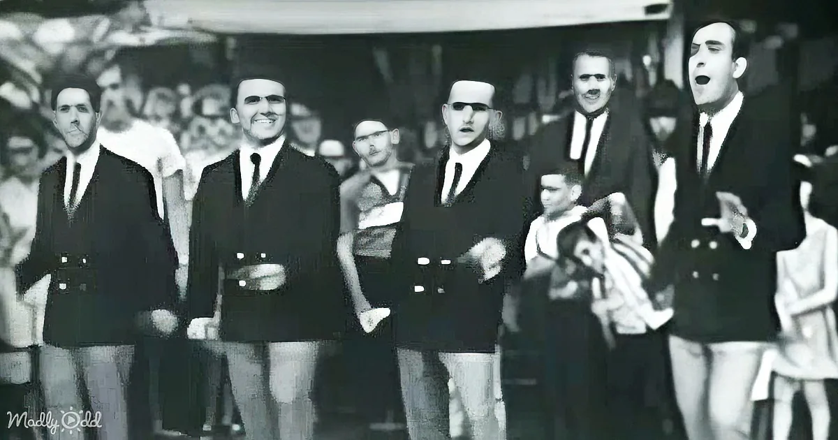 A group of men in suits and ties, some with mustaches, are singing or speaking in a public setting.