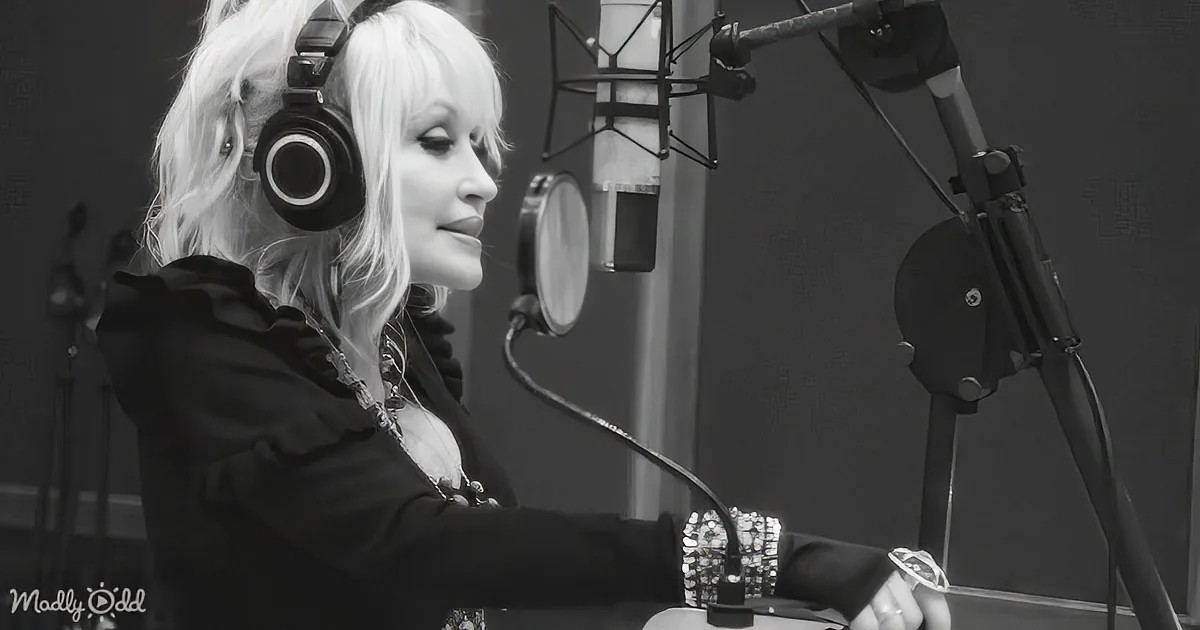 A person with white hair and headphones is in a recording studio, focused on a microphone.
