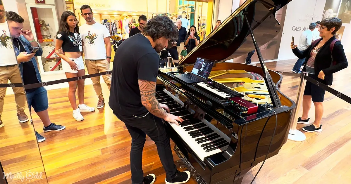 A man plays a grand piano with a laptop, surrounded by onlookers in a store.