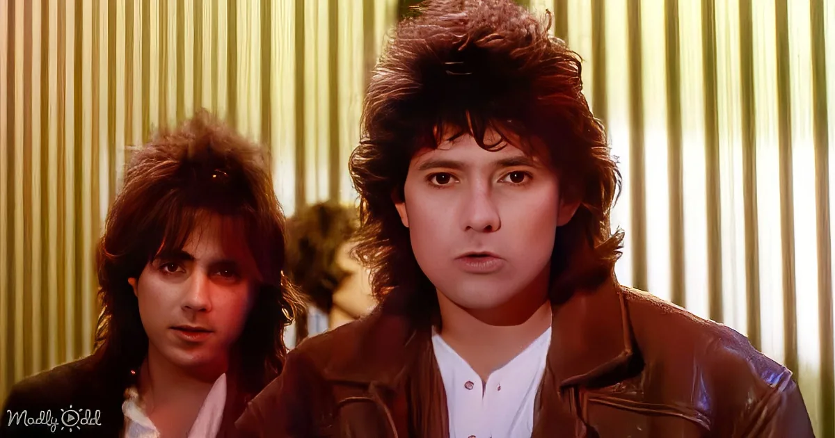 A man with a 1980s hairstyle and leather jacket stands in front of another person with similar hair, both against a...