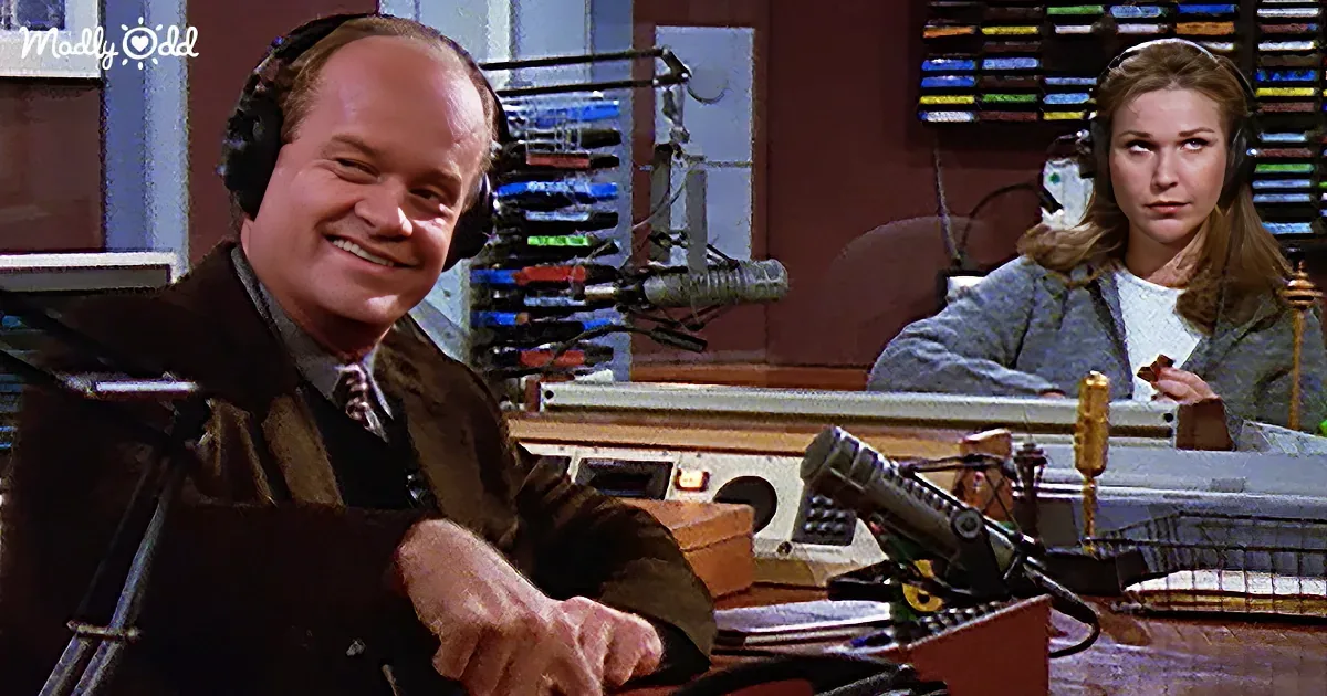 A man wearing headphones smiles while sitting at a desk with a woman in the background, both in a radio studio setting.