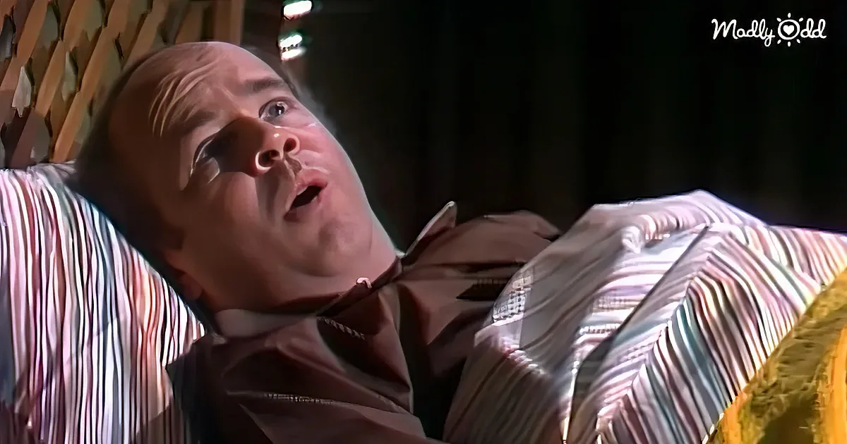 A man in a striped shirt and brown jacket is lying down, looking up with a surprised expression.