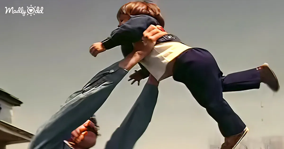 A man in a suit lifts a woman in a white blouse and dark pants, both mid-air, against a clear sky.