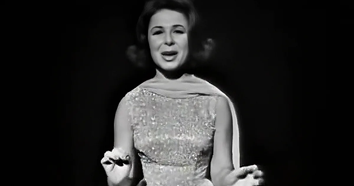 A woman in a white lace dress with her eyes closed, gesturing with her hands.