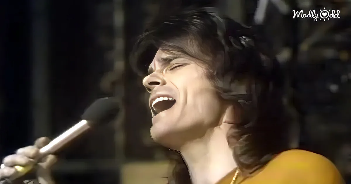 A person passionately sings into a microphone, their hair slightly tousled, with a microphone stand visible in the...