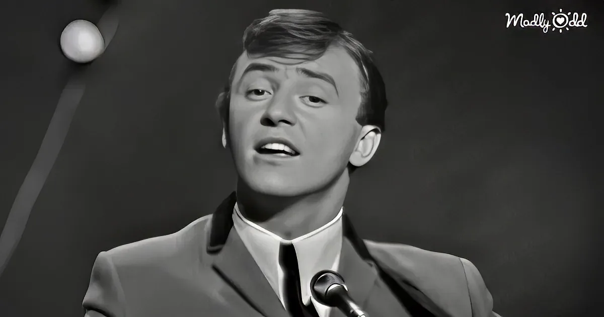 A man in a suit sings into a microphone, captured in a black-and-white close-up.