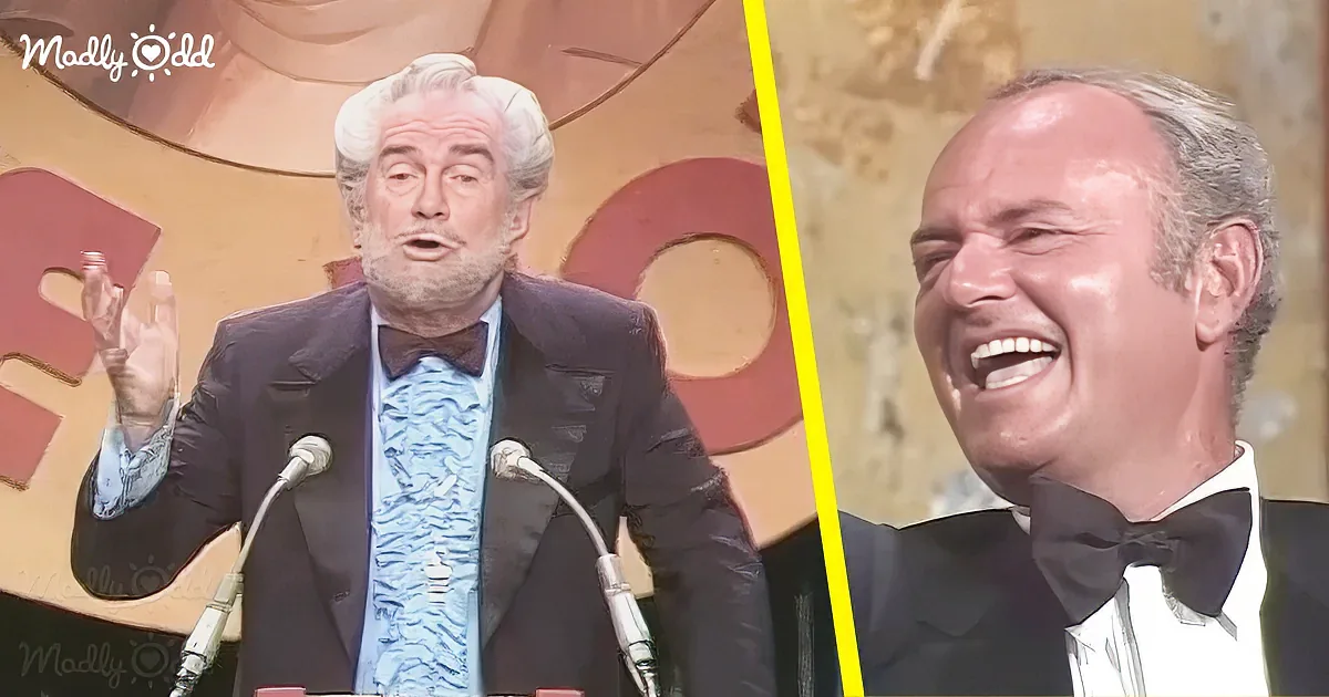 A man in a tuxedo is speaking at a podium, while another man in a tuxedo laughs beside him.
