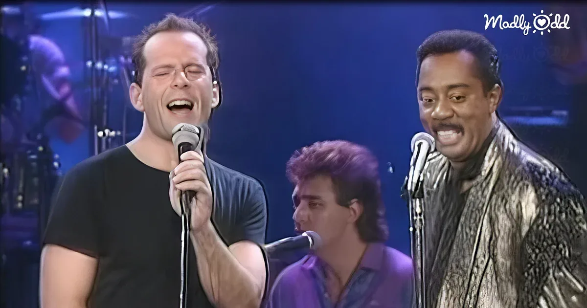 A man in a black shirt sings into a microphone, surrounded by other musicians on stage.