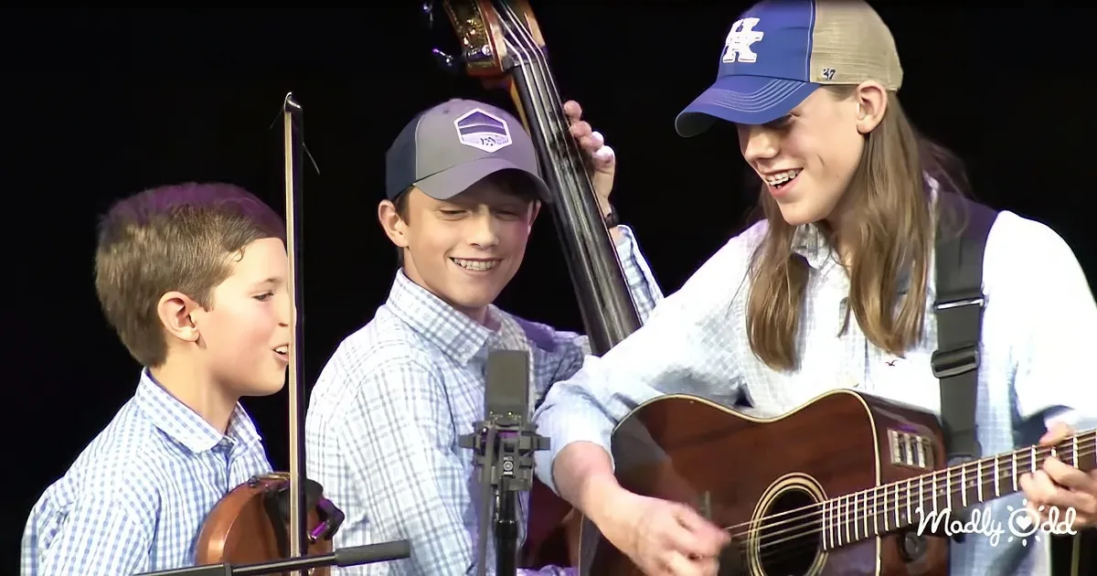 A girl plays guitar while a boy sings and another boy holds a bass.