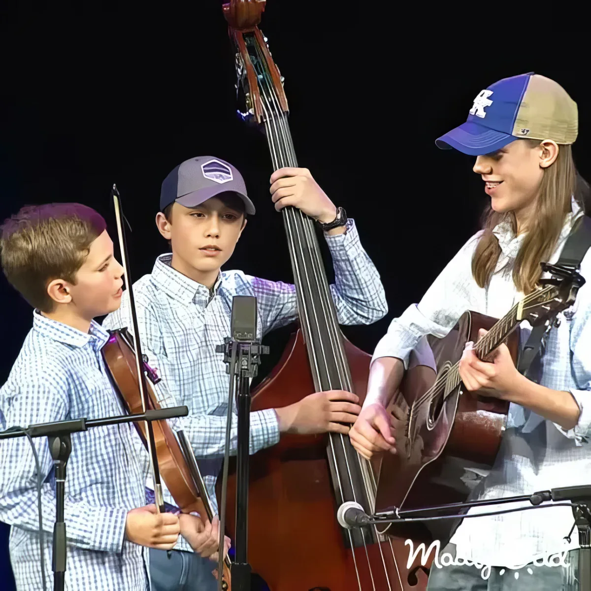 Young bluegrass brothers play banjo and fiddle on porch, concentrating on their music.