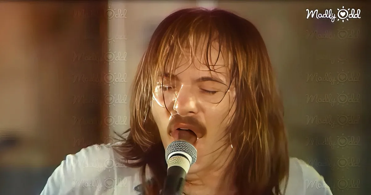 A person with long hair singing into a microphone, wearing a white shirt.