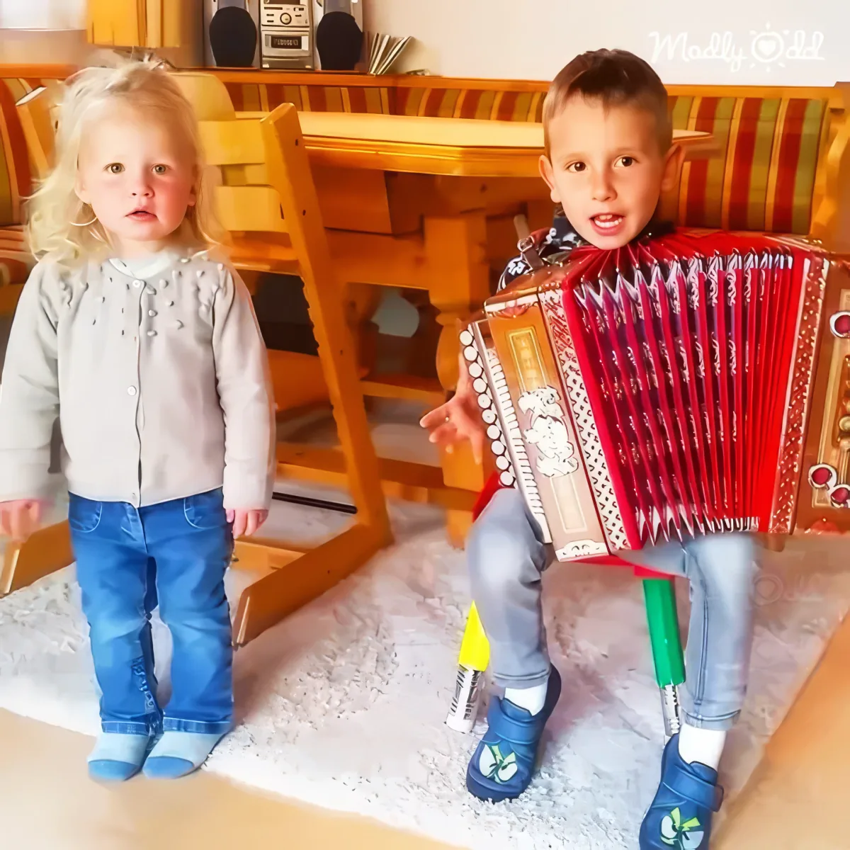 Tiny accordion player and dancing sister perform, audience captivated by their charm.