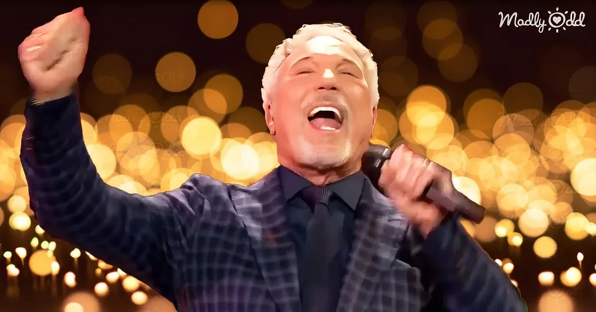 A man in a checkered suit sings passionately, raising his fist, against a backdrop of golden bokeh lights.