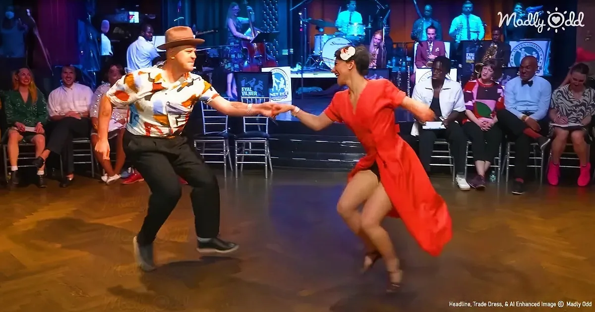 A man in a hat and colorful shirt dances with a woman in a red dress on a wooden floor, surrounded by an audience and a...