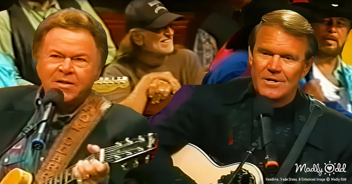 A man in a suit plays a guitar with a microphone in front of him, surrounded by people.