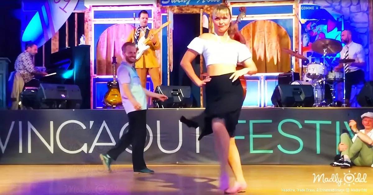 A woman in a white crop top and black skirt dances on stage at the Swing About Festival, with a band in the background.