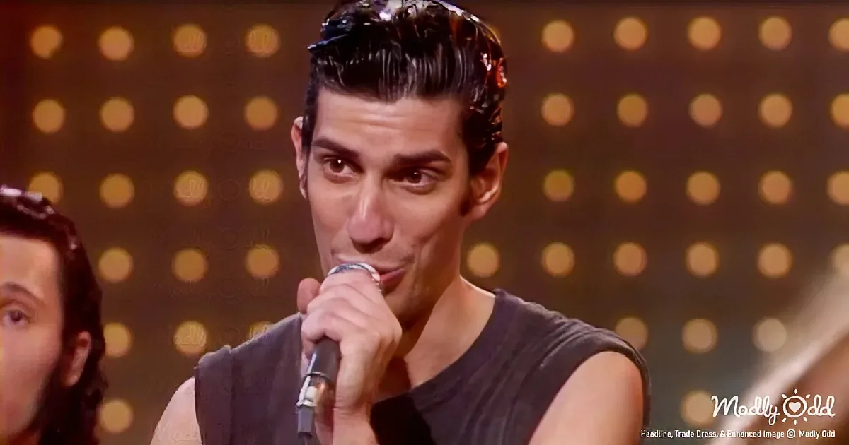 A man in a black sleeveless shirt sings into a microphone, with another person partially visible to his left.