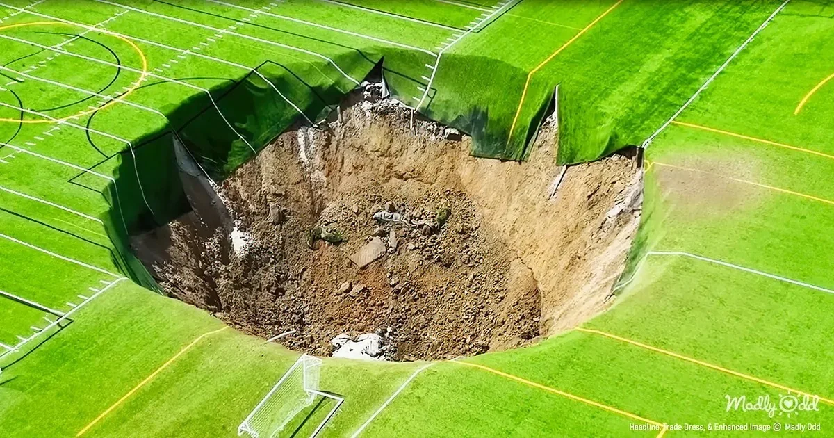 A large, deep hole in the middle of a football field, exposing dirt and debris.