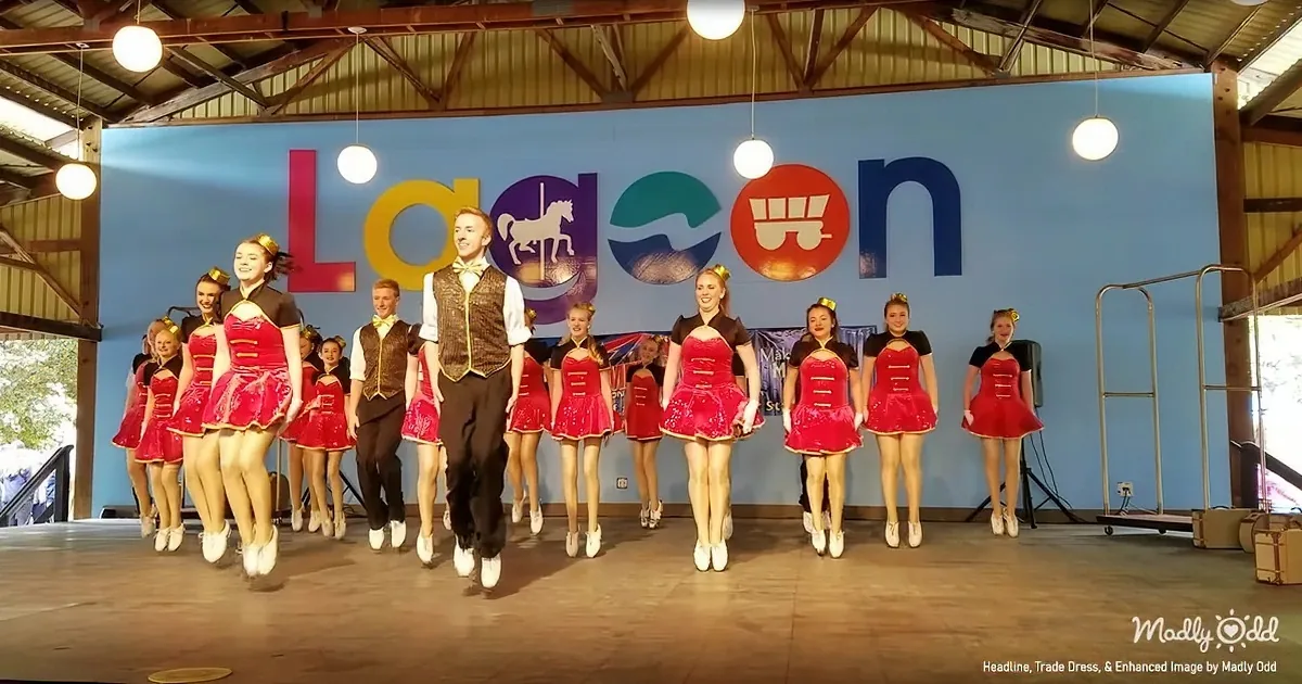 A man leads a group of dancers in red costumes on a stage with a "Lagoon" backdrop.
