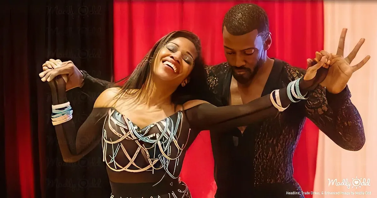 A couple in dance attire smiles and poses together, arms outstretched, against a red curtain backdrop.