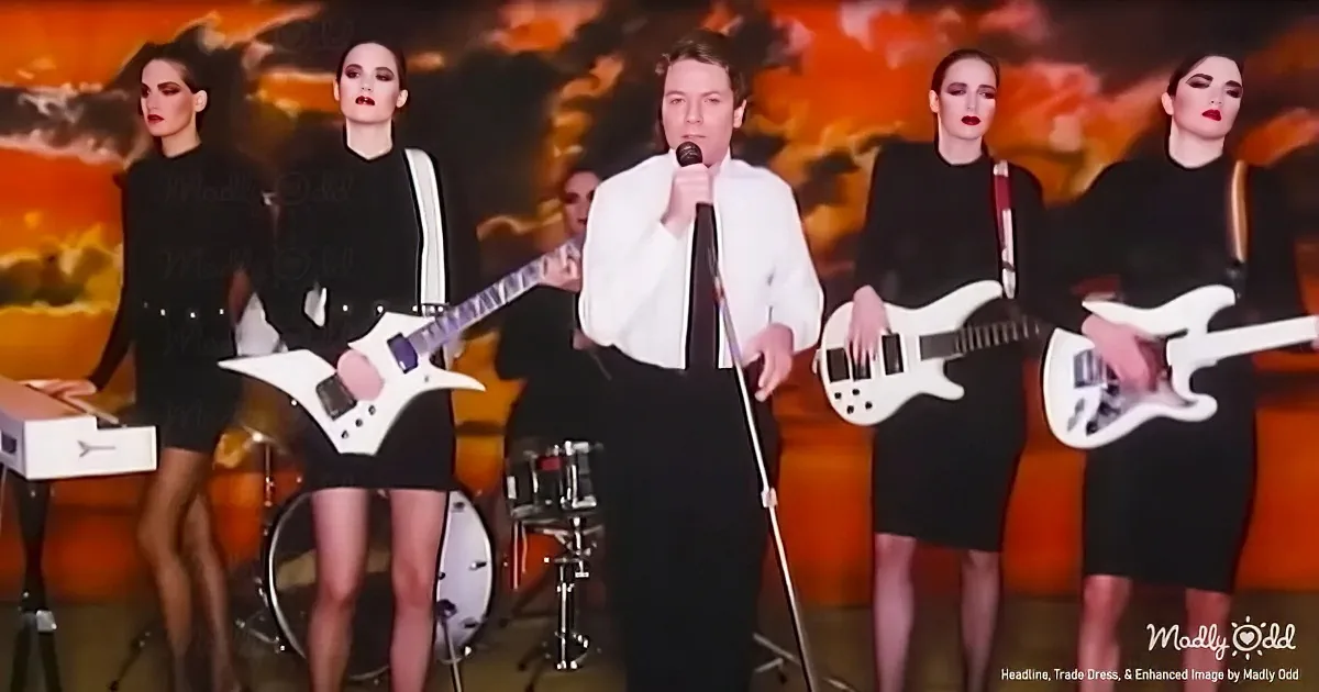 A man in white shirt sings into microphone, surrounded by four women in black dresses playing guitars.