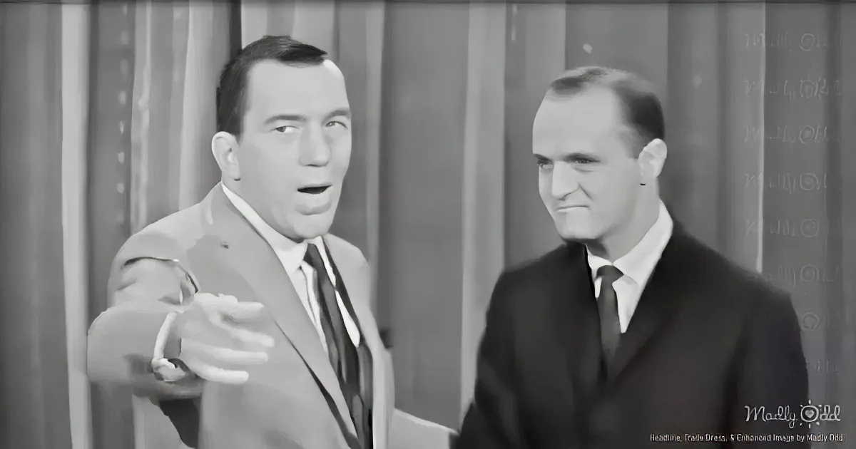Two men in suits, one gesturing, both in a formal setting, possibly a talk show or interview.