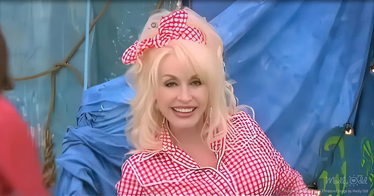 A woman with blonde hair, wearing a red and white checkered dress and a red polka dot headband, smiles in front of a blue...