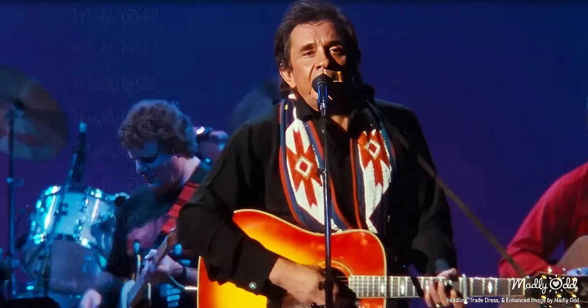A man in a black jacket with a red and white patterned scarf plays a yellow guitar and sings into a microphone.