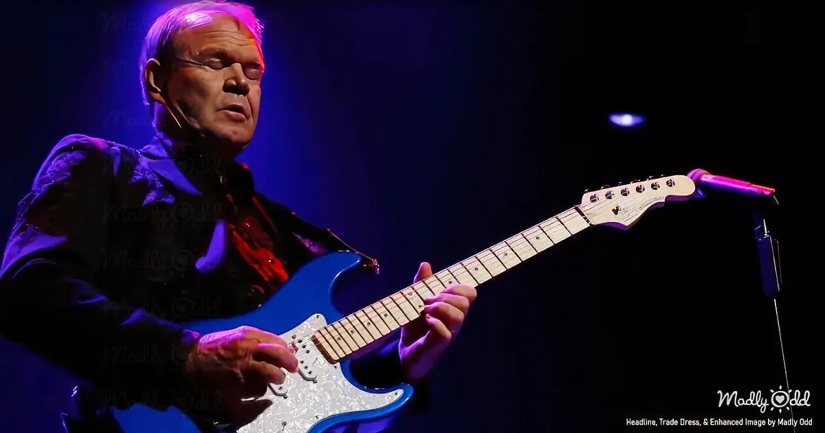 A man plays a blue electric guitar on stage under purple lighting.