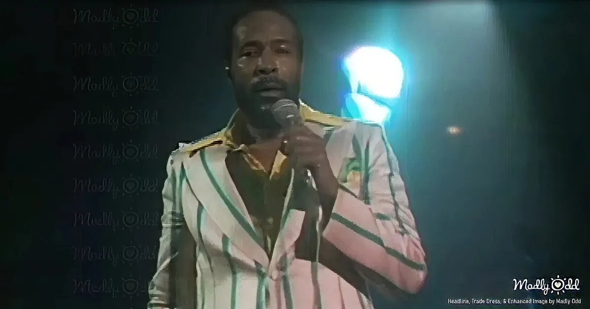 A man in a striped suit holds a microphone on stage under bright lights.