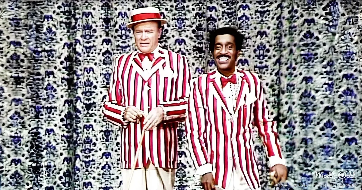 Two men in red and white striped suits stand against a patterned backdrop, one holding a cane.