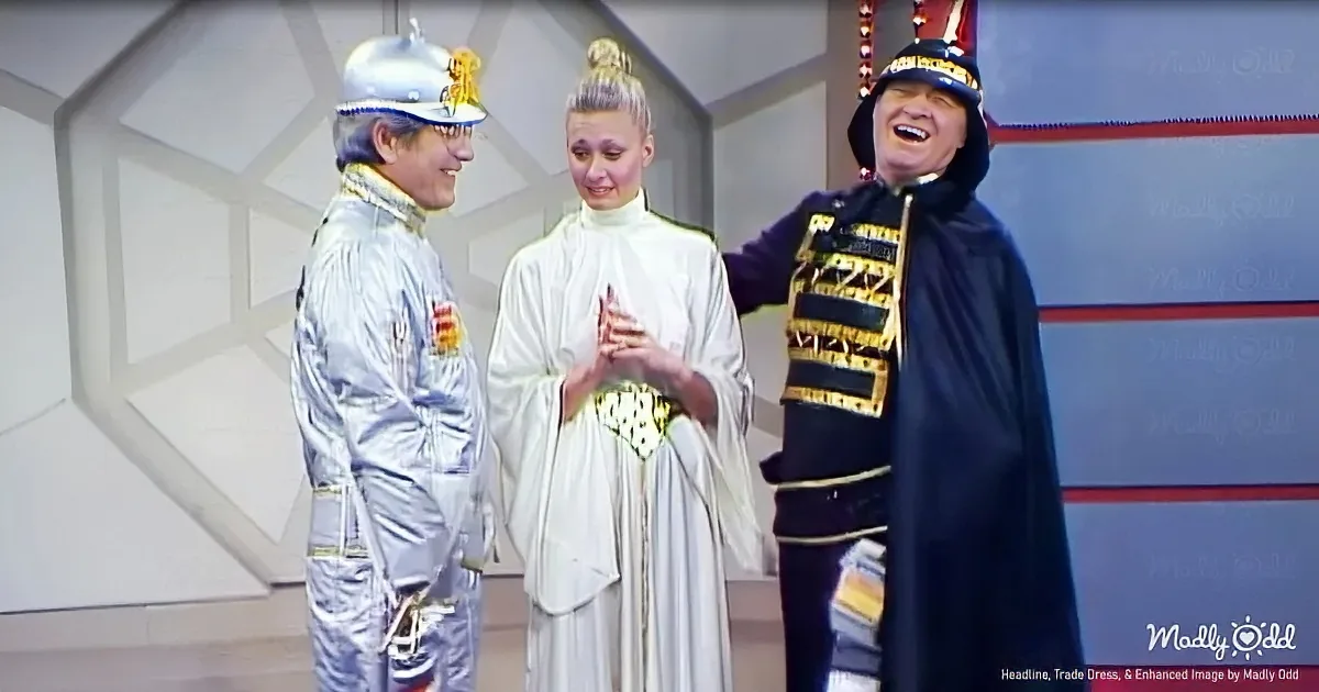 A man in a silver astronaut suit interacts with a woman in a white robe and another man in a black cape and hat.