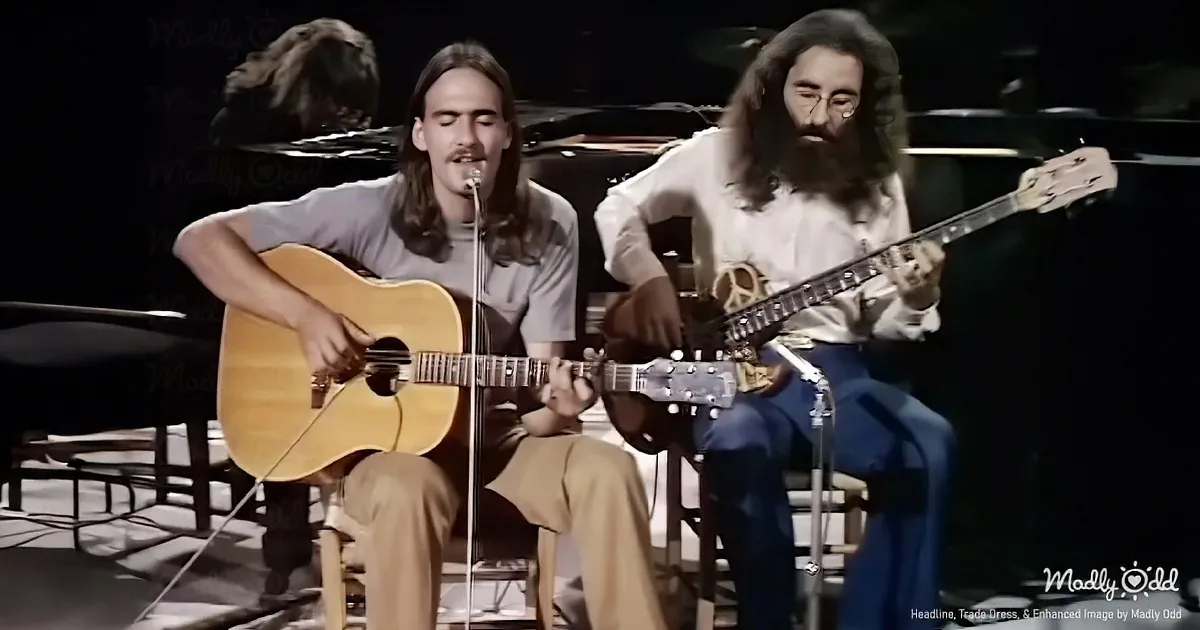 Two musicians with long hair play acoustic guitars on stage, one wearing a peace sign belt.