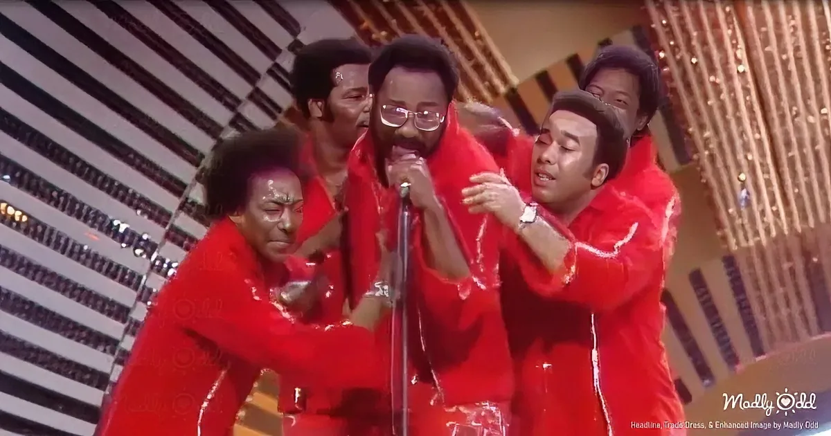 A man in red, holding a microphone, surrounded by others in red, performing on stage.