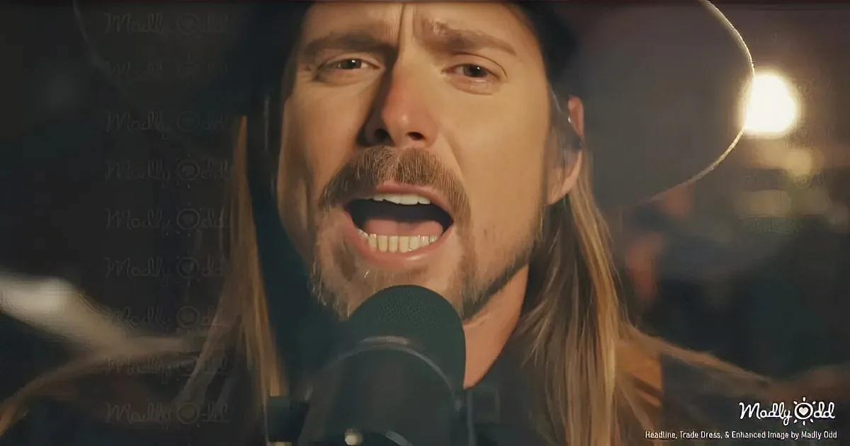 A man with long hair and a hat sings into a microphone, illuminated by a warm light.