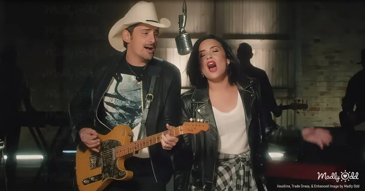 A man in a cowboy hat and a woman in a leather jacket sing and play guitar together.