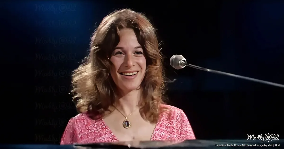 A smiling woman with shoulder-length brown hair, wearing a pink patterned top and a necklace, stands in front of a...