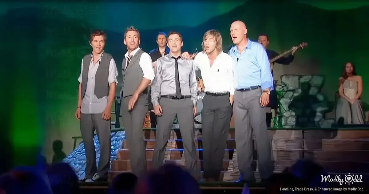 A group of men in formal attire sing on stage, accompanied by musicians and a backdrop.