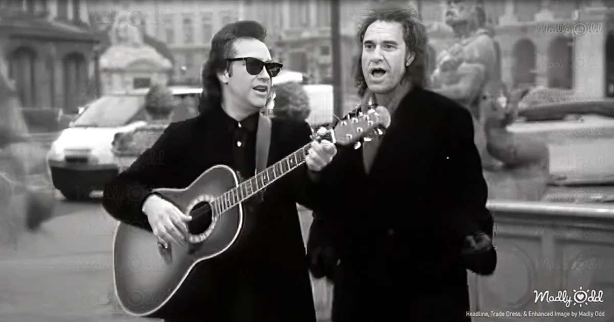 Two men, one playing guitar, singing in a black-and-white urban setting with statues and cars.