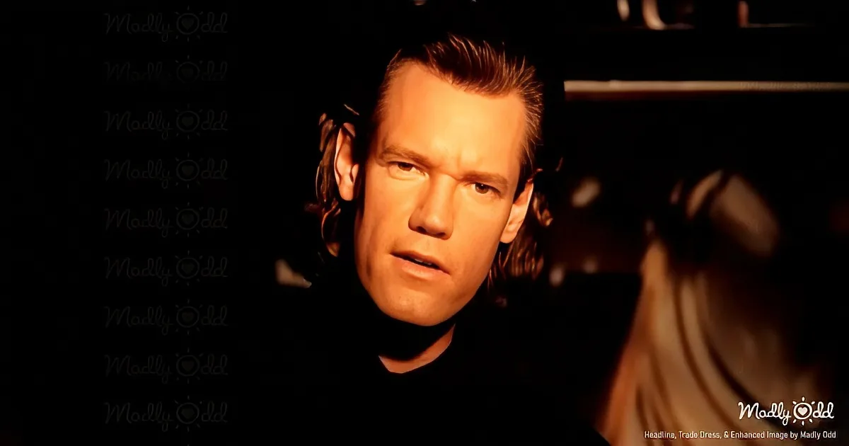 A man with short hair and a serious expression, wearing a dark turtleneck, is shown in a dimly lit setting.