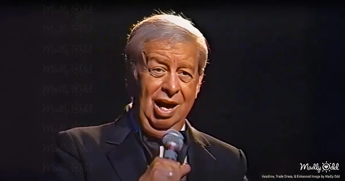 A man in a suit speaks into a microphone, wearing a white head covering, against a dark background.