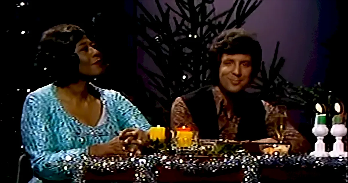 Two individuals sit at a table adorned with candles and decorations, engaged in conversation.