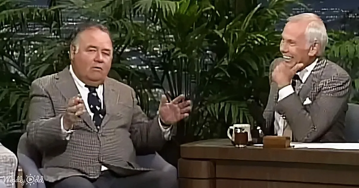 A man in a suit gestures animatedly while seated, engaging in a conversation with another man laughing.