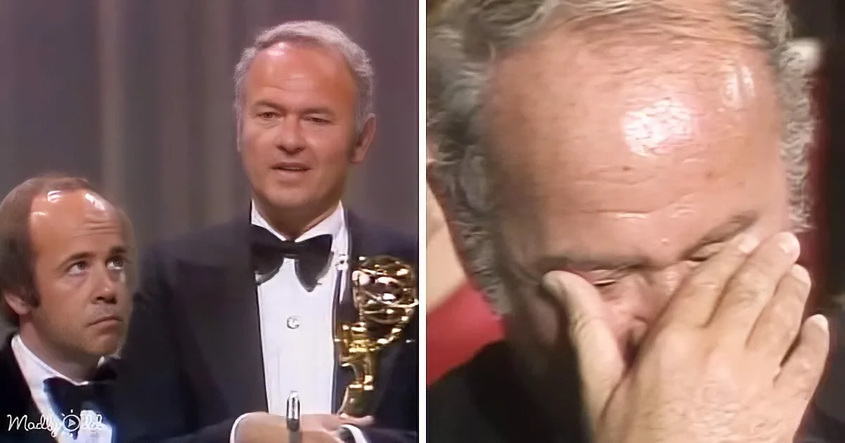 A man in a tuxedo holds an Emmy award, while another man in a tuxedo looks on with a concerned expression.