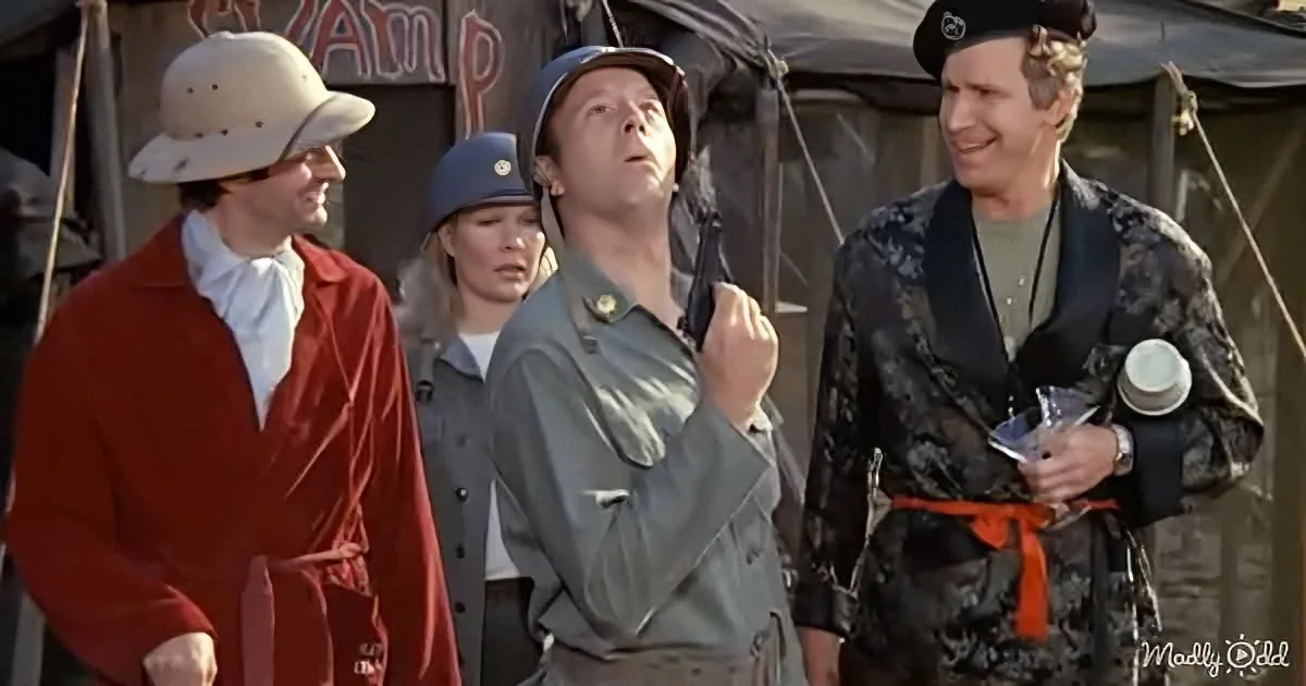 A man in a safari outfit looks up, surrounded by others in various costumes, in a camp setting.