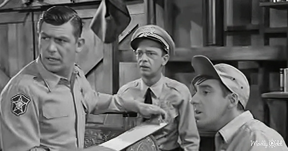 A man in a sheriff's uniform adjusts another man's tie while a third man in a cap looks on.