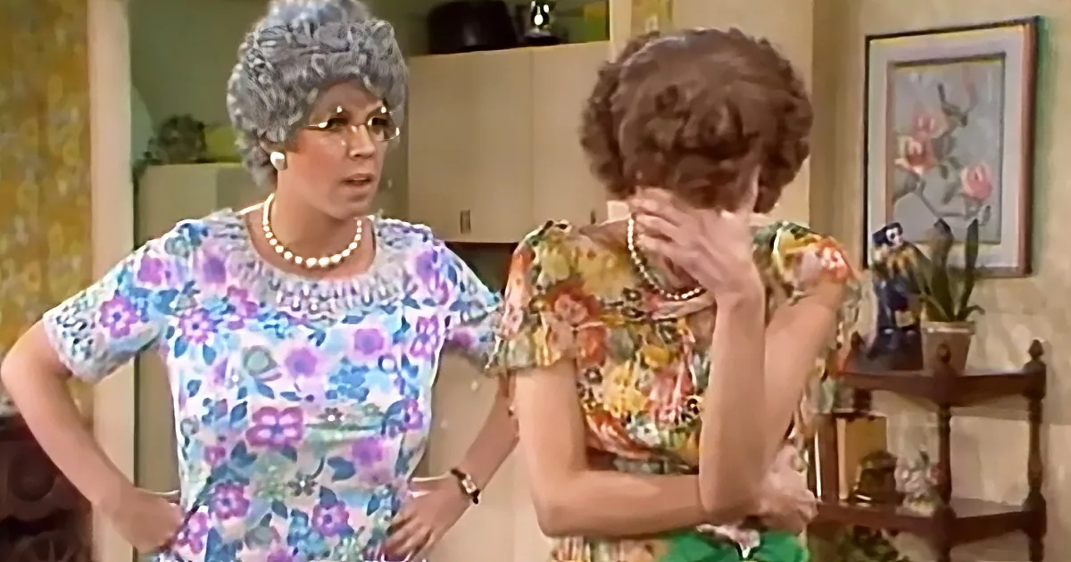 A woman in a floral dress with a pearl necklace stands with hands on hips, while another woman in a floral dress covers...