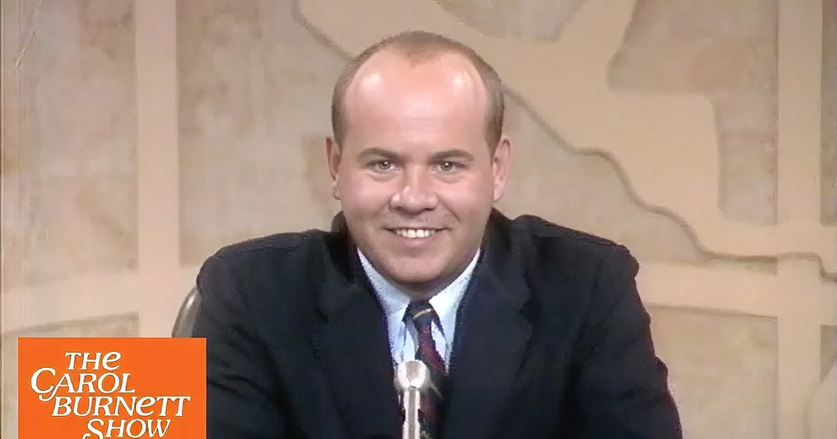 A man in a suit and tie is smiling while sitting in front of a microphone.